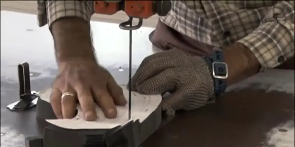 A cutter guiding layered fabric through a band knife, wearing a steel mesh glove