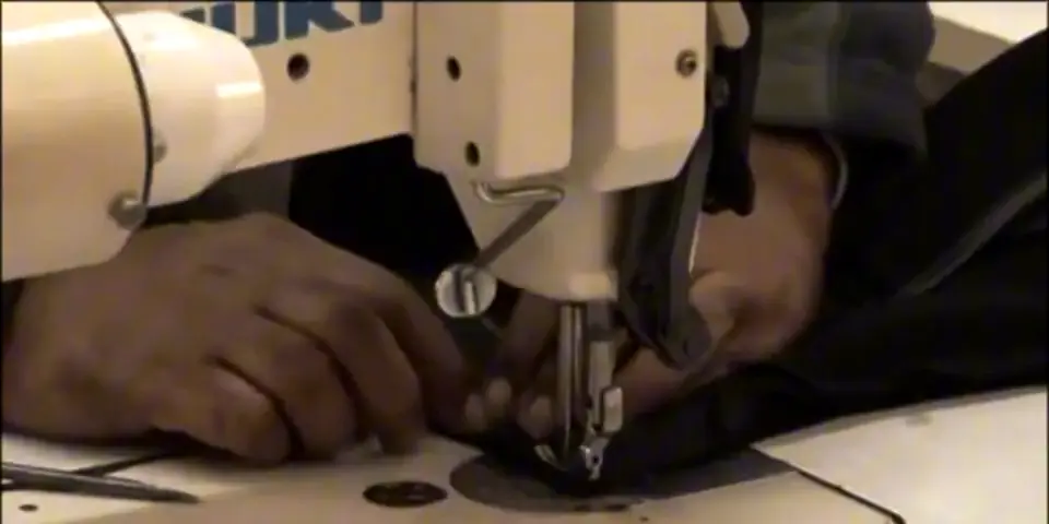 Hands guiding fabric under an industrial sewing machine